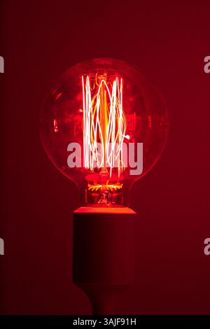 A glowing vintage lightbulb with intricate filaments, bathed in a deep red hue. Stock Photo