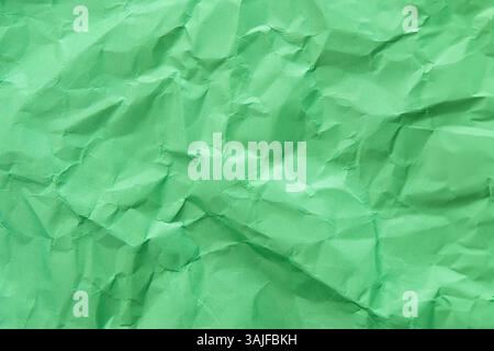 A close-up, top-down shot showcases the crinkled and uneven texture of green paper. Background concept. Stock Photo