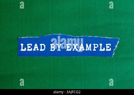 Lead by example message written on ripped torn blue paper piece on green background. Conceptual lead by example symbol. Copy space. Stock Photo
