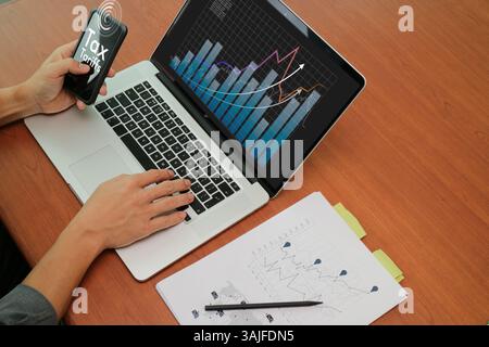 Hands working on a laptop and holding a smartphone with charts and graphs displaying tax and tariffs growth trends. Stock Photo
