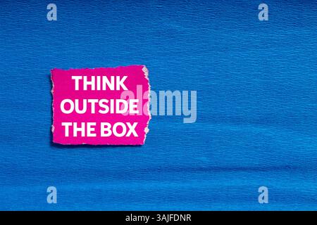Think outside the box message written on ripped torn pink paper on blue background. Conceptual think outside the box symbol. Copy space. Stock Photo