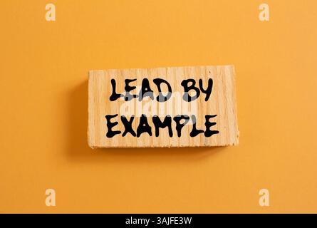Lead by example message written on wood piece on orange background. Conceptual lead by example symbol. Copy space. Stock Photo