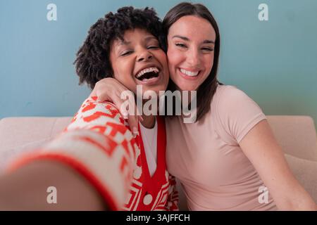 Two happy women taking a fun selfie together while sitting on a couch at home Stock Photo