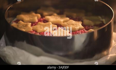 Raw raspberry pie with star-shaped shortcrust pastry on top baking in metal cake ring. Studio food photography. Holiday dessert preparation. Christmas Stock Photo