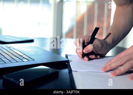 office worker working on laptop, taking notes on paper, notes, technology development, data processing Stock Photo