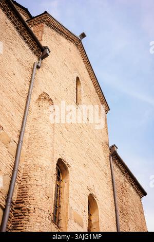 Upward view of an ancient brick church wall with arched windows and textured masonry, lit by warm sunlight. Captured in Georgia, evoking historical de Stock Photo