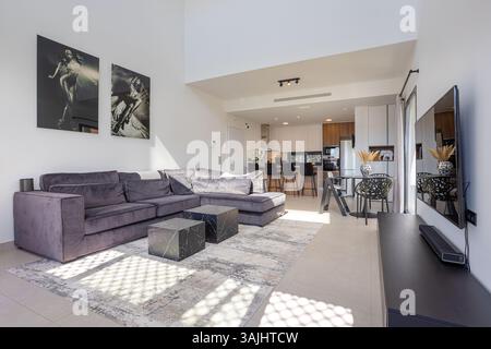 A spacious and stylish open plan living area featuring a velvet sectional sofa, contemporary kitchen, bar stools, and black and white wall art under h Stock Photo