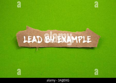 Lead by example message written on ripped torn brown paper piece on green background. Conceptual lead by example symbol. Copy space. Stock Photo