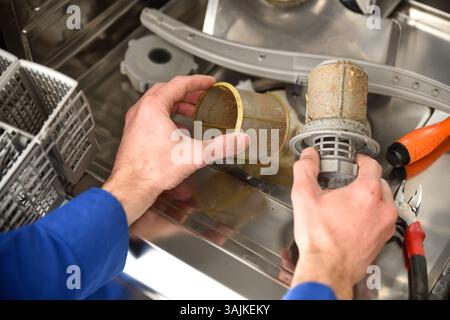 Detail of a technician's hands with dirty parts of a dishwasher performing maintenance with tools around. Elevated view. Stock Photo