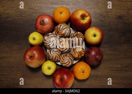 Cakes on a saucer surrounded by fruits - apples, oranges, pomegranates. Top view. Stock Photo