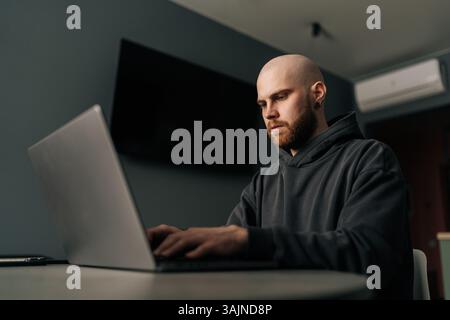 Concentrated male programmer in casual clothes typing code on laptop, developing software in home office environment, focused looking to screen. Stock Photo