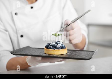Confectioner decorating tasty tart with mint at grey table in kitchen, closeup Stock Photo
