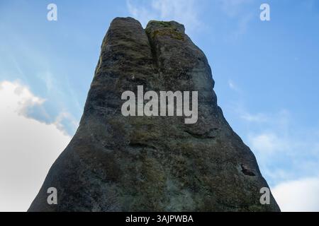 A large rock with moss growing on it. The sky is blue and there are some clouds. The rock is tall and has a unique shape Stock Photo