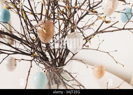 Easter tree decorated colorful pastel white and beige eggs. Birch branches with hang eggs in vase on white table. Close up Stock Photo