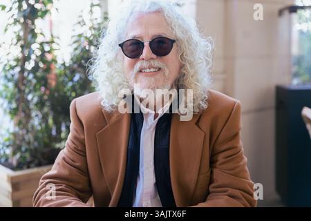 Stylish senior man with white curly hair and sunglasses sitting at outdoor cafe Stock Photo