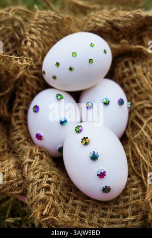 Beautifully arranged hand-decorated Easter eggs featuring floral sequin patterns in a pink bowl and jute wrapping, photographed in a natural outdoor s Stock Photo