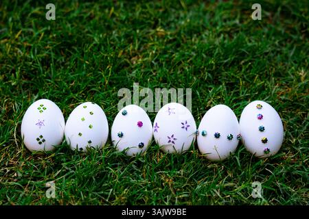 white Easter eggs adorned with colorful sequins and arranged on green grass, perfect for spring or Easter-themed content. Stock Photo