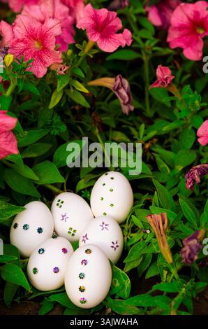 Beautifully decorated white Easter eggs placed on lush green grass, encircled by colorful spring flowers, capturing the festive essence of Easter in n Stock Photo