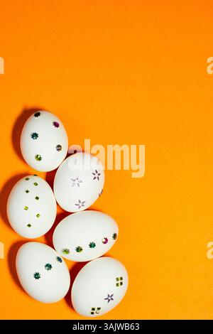 Minimalist Easter concept with white eggs embellished with colorful decorations, arranged on a bold orange backdrop for a clean, modern festive look. Stock Photo