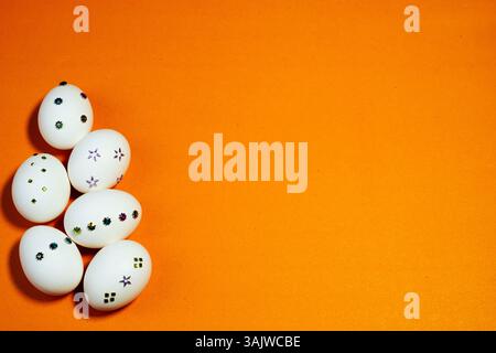 White eggs adorned with floral and geometric sequins laid on a solid orange background, ideal for banners, cards, ads, or seasonal marketing. Stock Photo