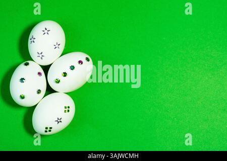 White eggs with colorful sparkle decorations displayed over vibrant Green paper, perfect for Easter-themed designs and seasonal marketing. Stock Photo
