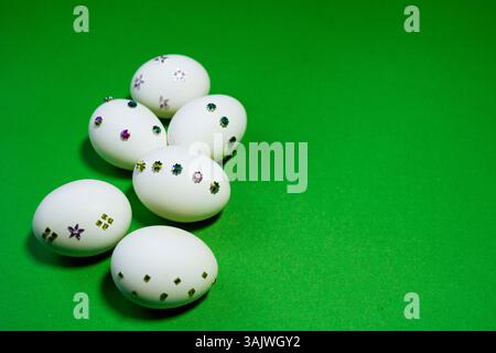Eye-catching Easter concept with shiny decorations placed on eggs and contrasted against a vivid green background. Stock Photo