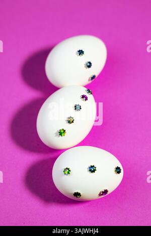 Easter Celebration Concept with White Sparkly Eggs Displayed On purple Background. Vibrant image of Easter eggs decorated with small shiny patterns pl Stock Photo