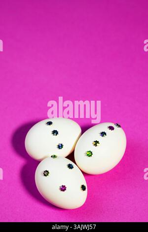 Easter-themed flat lay showing handmade white eggs with gems over a solid Pink surface, offering a modern and festive vibe. Stock Photo