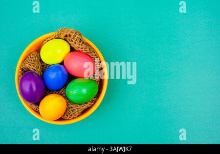 Easter Flat Lay with Multicolor Eggs in Rustic Bowl on Blue Background. Top view photo of festive colored eggs placed inside a textured bowl with deco Stock Photo