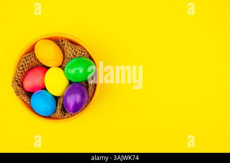 Warm-toned Easter photo featuring a rustic bowl of colorful eggs, placed on a glowing yellow backdrop for festive vibes. Stock Photo