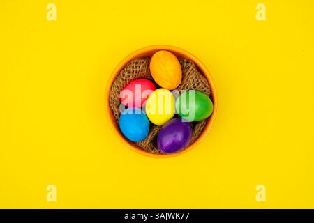 Decorated eggs resting in a natural bowl, styled with wooden threads, displayed over a bold yellow setup. Stock Photo