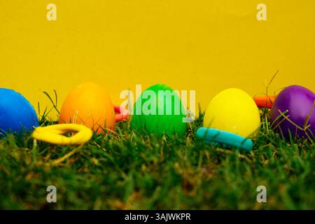 Bright multicolored eggs partially hidden in fresh green grass, set against a warm yellow background, symbolizing spring, Easter fun, and egg hunts. Stock Photo