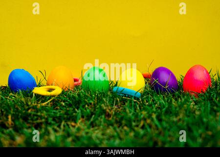 Decorated Easter eggs nestled in lush green grass, creatively styled with a cheerful yellow background for seasonal, festive, and spring-themed visual Stock Photo