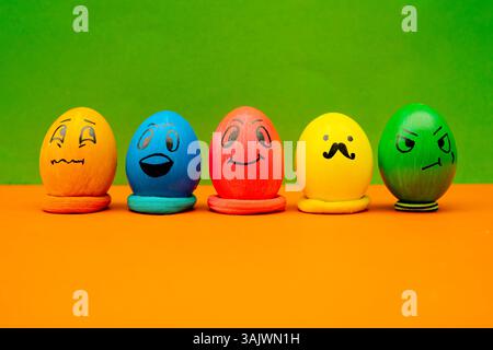 Lined Up Painted Easter Eggs With Expressive Cartoon Faces On Green and Orange Background. Playful spring-themed eggs with character designs on a bold Stock Photo