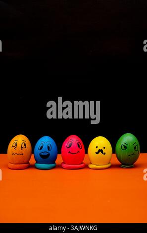 Five vibrant Easter eggs featuring hand-drawn emoji expressions, arranged neatly on an orange base with a dramatic black backdrop. Ideal for humor, cr Stock Photo