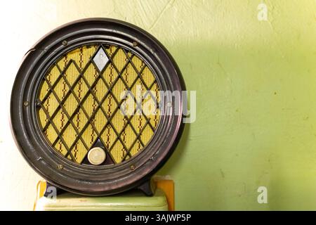 A round vintage radio is displayed against a light green wall. The radio features a diamond-patterned yellow mesh, adding a nostalgic touch. It evokes Stock Photo