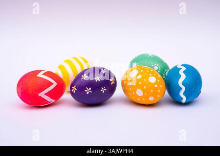 Six vibrant Easter eggs decorated with stripes, dots, and flowers resting on a plain white background for holiday themes. Stock Photo