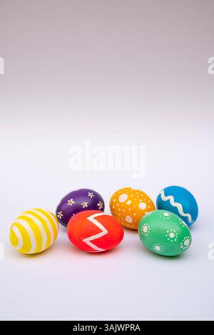 A creative Easter setup with hand-painted eggs in vivid colors and patterns arranged on a white studio backdrop. Stock Photo