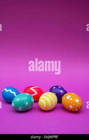 Vibrant Easter eggs decorated with different patterns, styled over a pastel pink surface for a festive vibe. Stock Photo