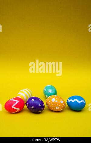 Beautiful hand-painted eggs in purple, yellow, blue, green, red, and orange arranged on a yellow surface for Easter celebrations. Stock Photo