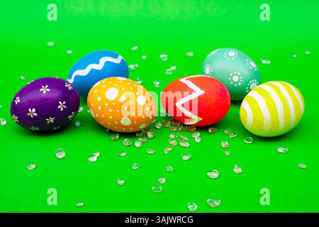Colorful Designed Easter Eggs Lying on Vibrant Green Background. A group of bright, hand-painted Easter eggs placed on a clean green surface, perfect Stock Photo