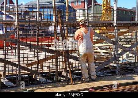 A worker in overalls and a hard hat is busy making reinforcement mesh or frame for use in reinforced concrete building structures in Nuuk, Greenland Stock Photo