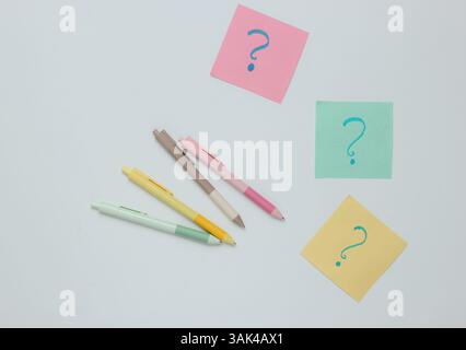 Pens and memo piece of paper with question marks on white background. Top view Stock Photo