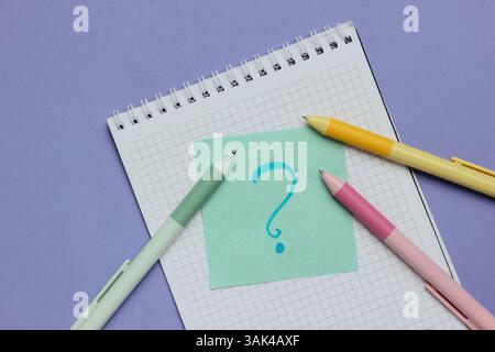 Notepad with pens and memo piece of paper with question mark on purple background. Top view Stock Photo