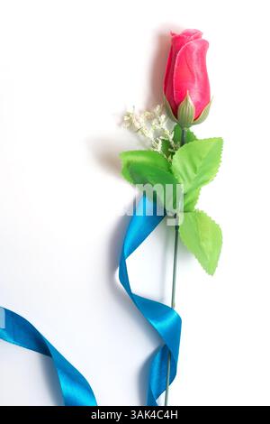 An artificial red rose with bright green leaves and a blue ribbon, elegantly displayed against a bright white background, evokes themes of romance and Stock Photo