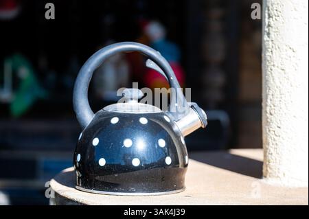 A black kettle with white polka dots sits on a rustic surface, illuminated by sunlight. Stock Photo