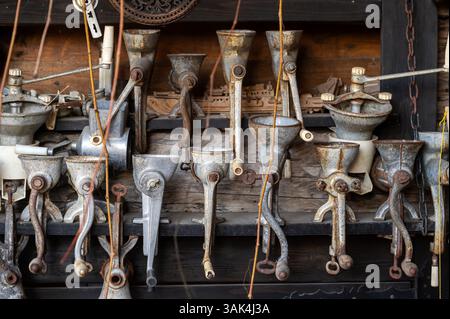 Various antique food grinders are neatly arranged on a weathered wooden shelf in a workshop. Stock Photo