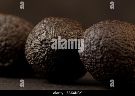 several whole black avocado fruits of small size on a black slate, ripe avocado fruit for cooking, closeup Stock Photo