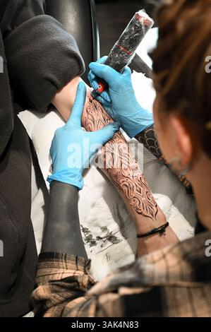 Tattoo artist carefully drawing a black ink tattoo on a client's arm, creating permanent body art Stock Photo
