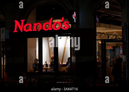 Exterior of a suburban Nando's restaurant at night, with brightly illuminated signage and patrons visible Stock Photo